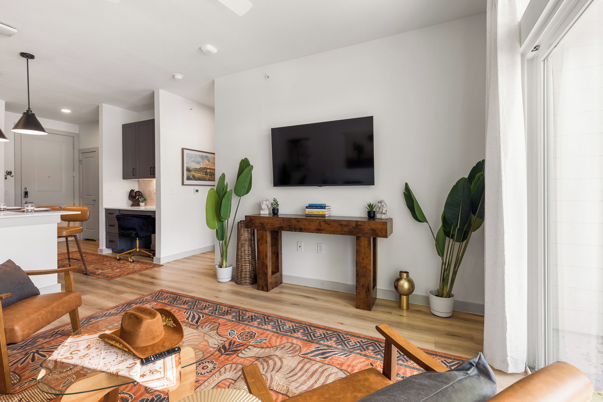 A modern living room with a flat-screen TV, a wooden console table, and large green plants.