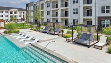 A modern apartment building with a swimming pool, outdoor seating, and a fenced garden area.