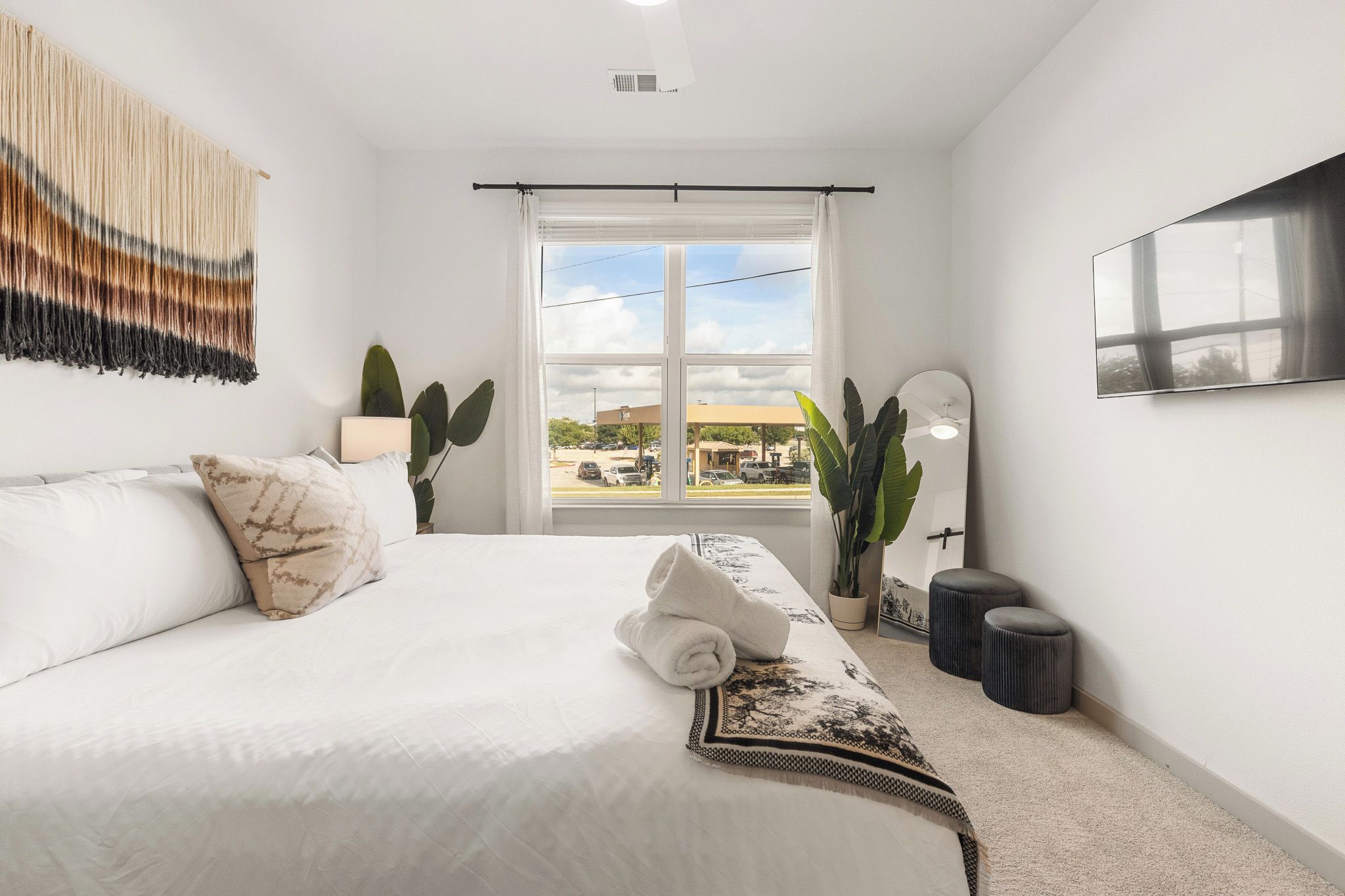 A hotel room with a large bed, a TV, a window with a view of the outside, and a plant.