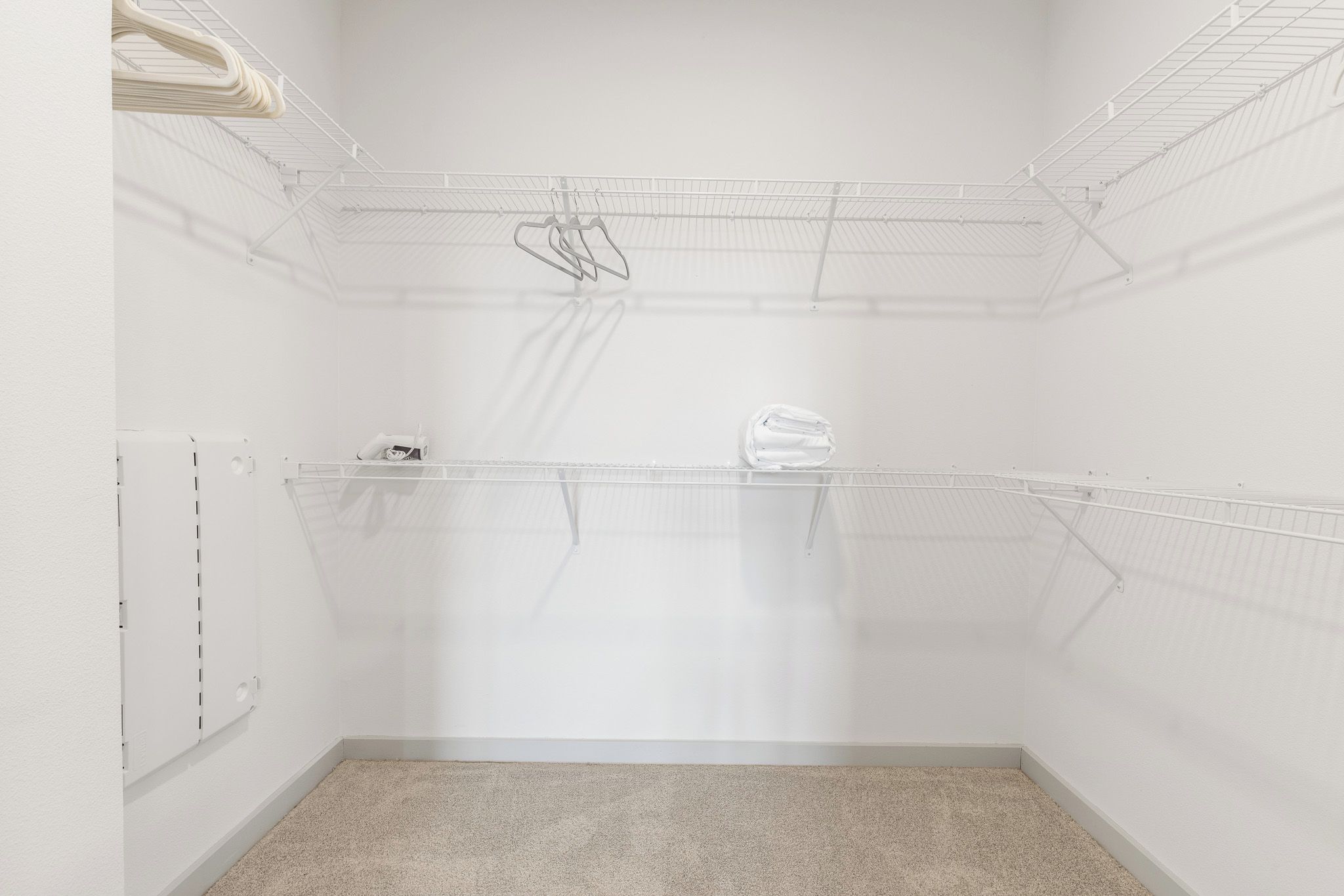 A small, empty walk-in closet with a metal shelving unit, a white door, and a carpeted floor.