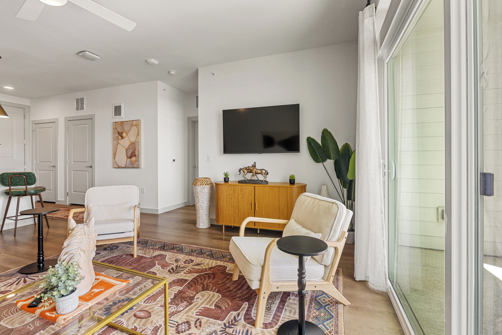 A modern living room with a flat-screen TV, a sofa, a chair, a coffee table, and a patterned rug.