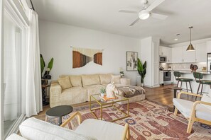 A spacious living room with a sofa, coffee table, and chairs, a kitchen area with white cabinets, and a ceiling fan. - Elegant 1BR Escape | Modern Comforts MER 2208 (San Marcos)