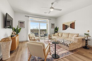 Een ruime woonkamer met een zithoek, een salontafel, een aan de muur bevestigde televisie en een balkon met uitzicht.