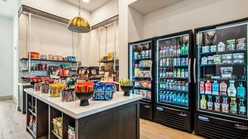 A well-stocked beverage refrigerator with various drinks, a central counter with snacks and packaged goods, and a hanging light fixture.