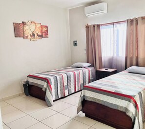 A hotel room with two beds, a window with curtains, an air conditioning unit, and a wall-mounted artwork. - Casa Madero #1, 1 block from the Malecón (La Paz)