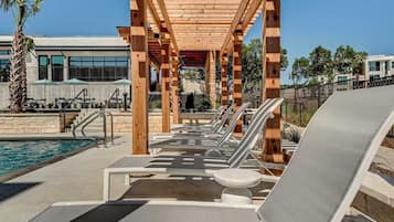 A poolside area with lounge chairs, a wooden pergola, and a view of a building in the background.
