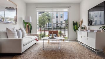 A modern living room with a sofa, coffee table, and a view of the outside through a sliding door.