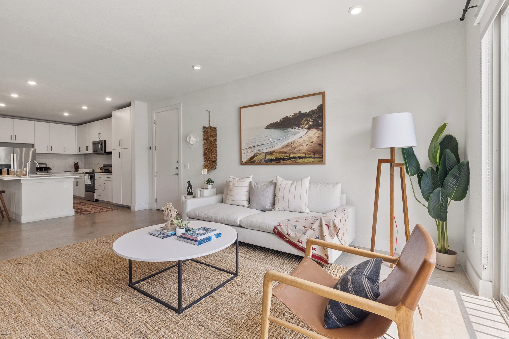 Una sala de estar moderna con sofá, mesa de centro y comedor, con una cocina al fondo.