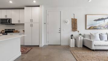 A modern kitchen with white cabinets, a microwave, and a dining area with a white table and chairs.