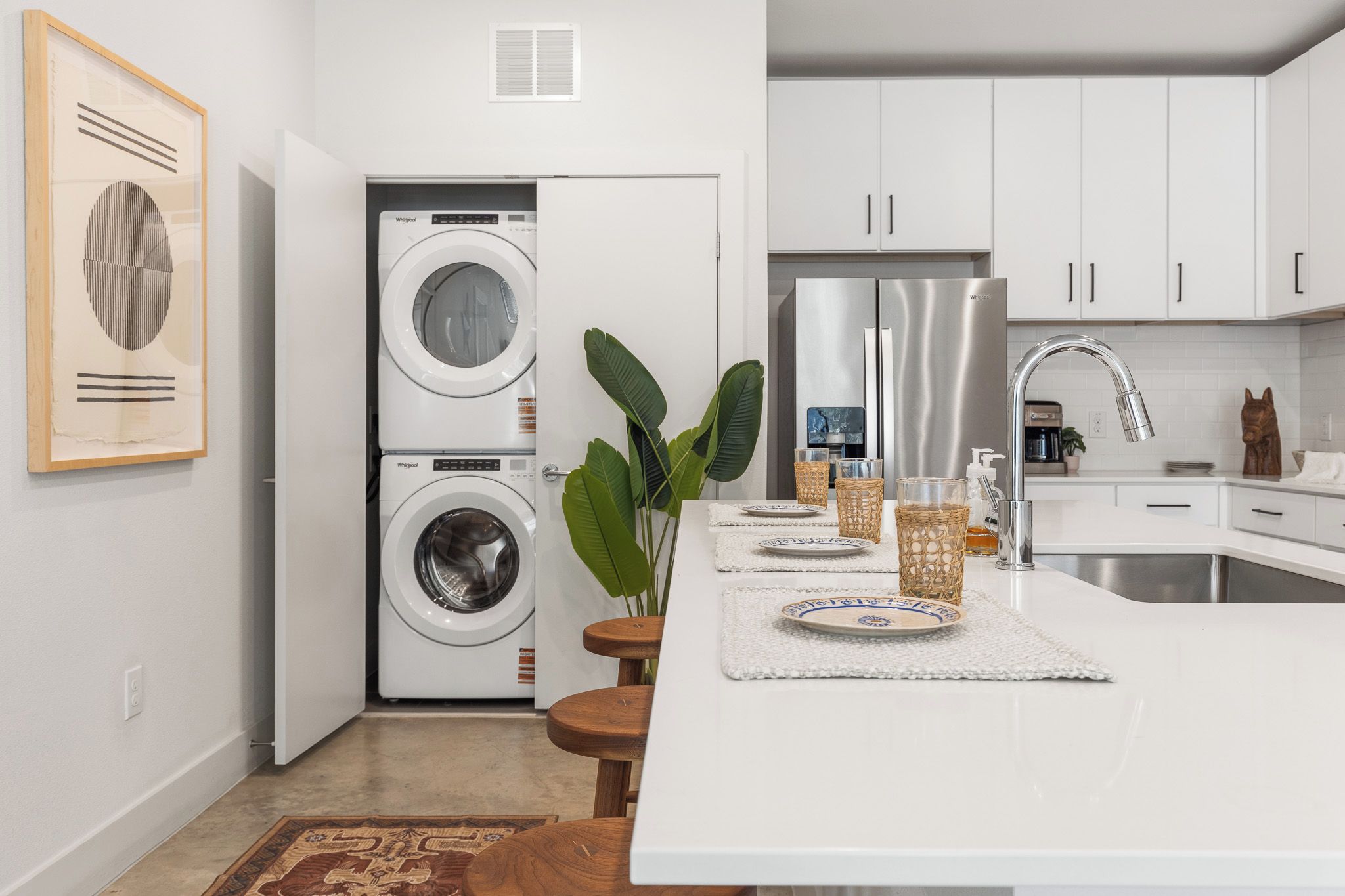 Une cuisine moderne dotée d’un lave-linge et d’un sèche-linge intégrés, d’appareils électroménagers en acier inoxydable et d’un îlot central avec un évier et des tabourets.