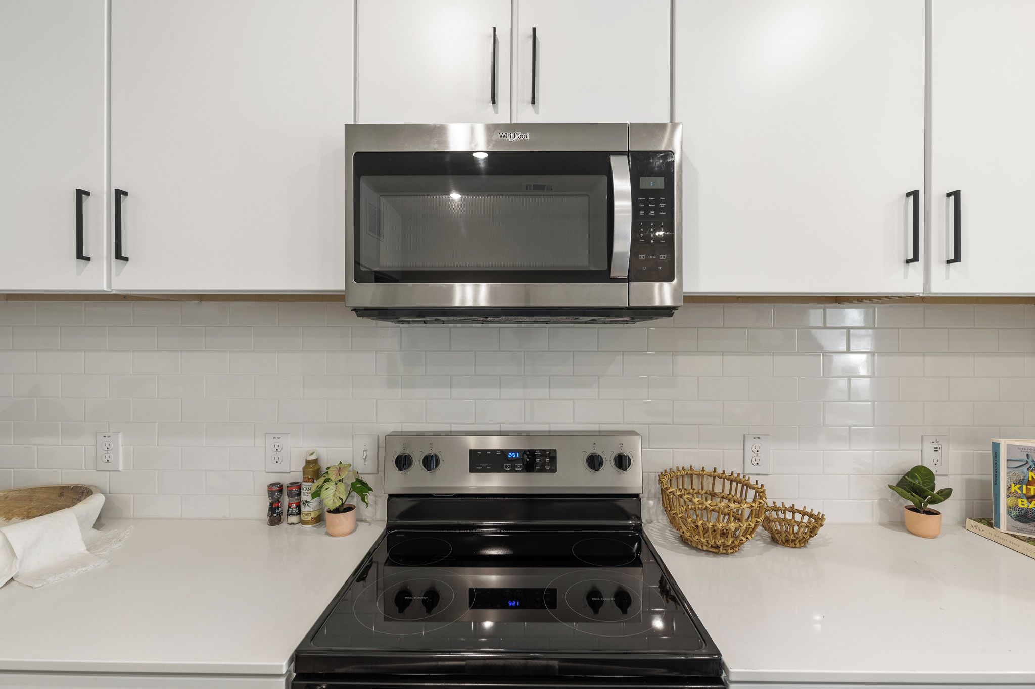 A kitchen with white cabinets, a stainless steel microwave, an oven, and a digital clock.