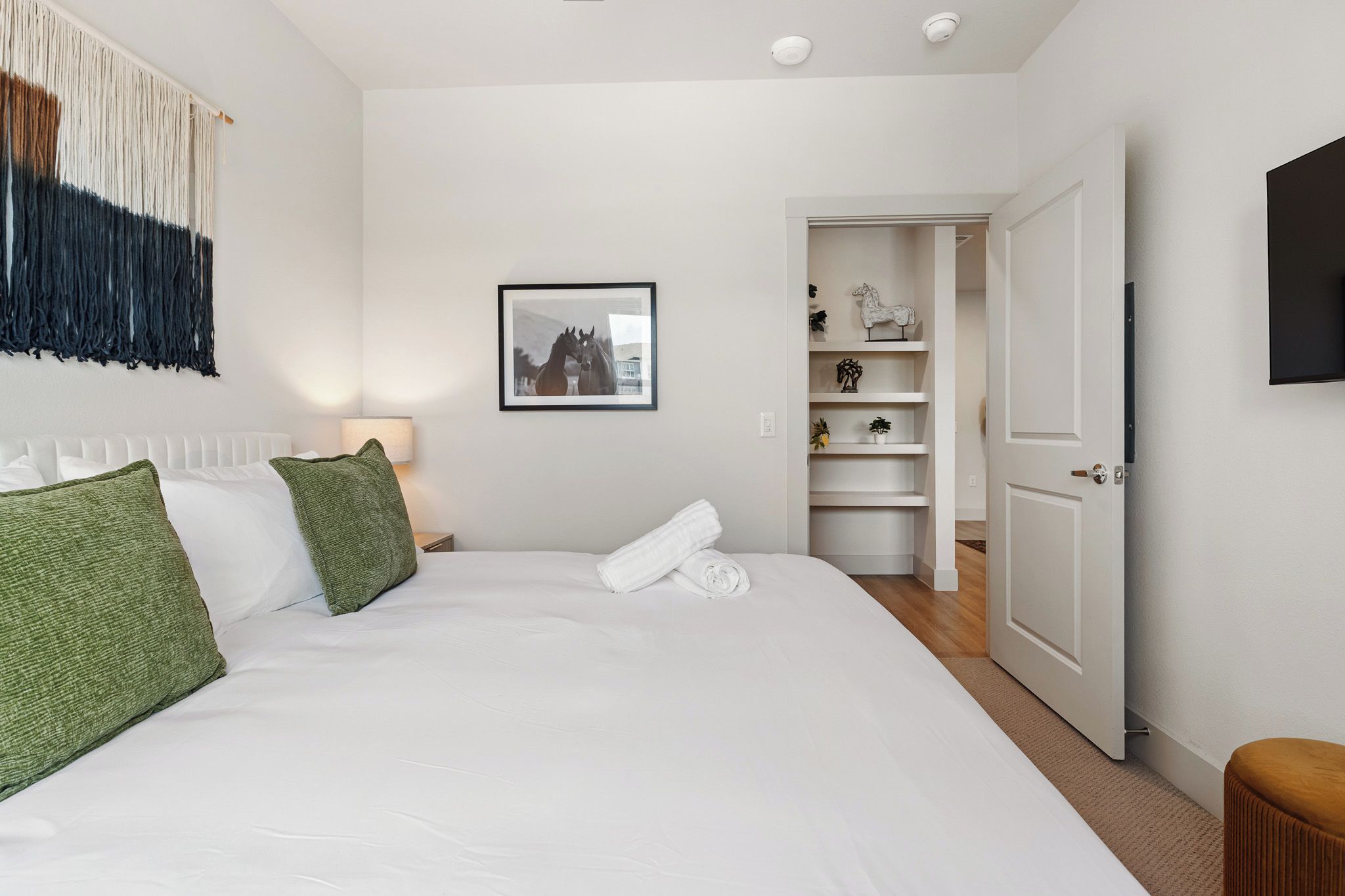 A hotel room with a large bed, a bedside table with a lamp, a framed picture on the wall, and a wardrobe with shelves.