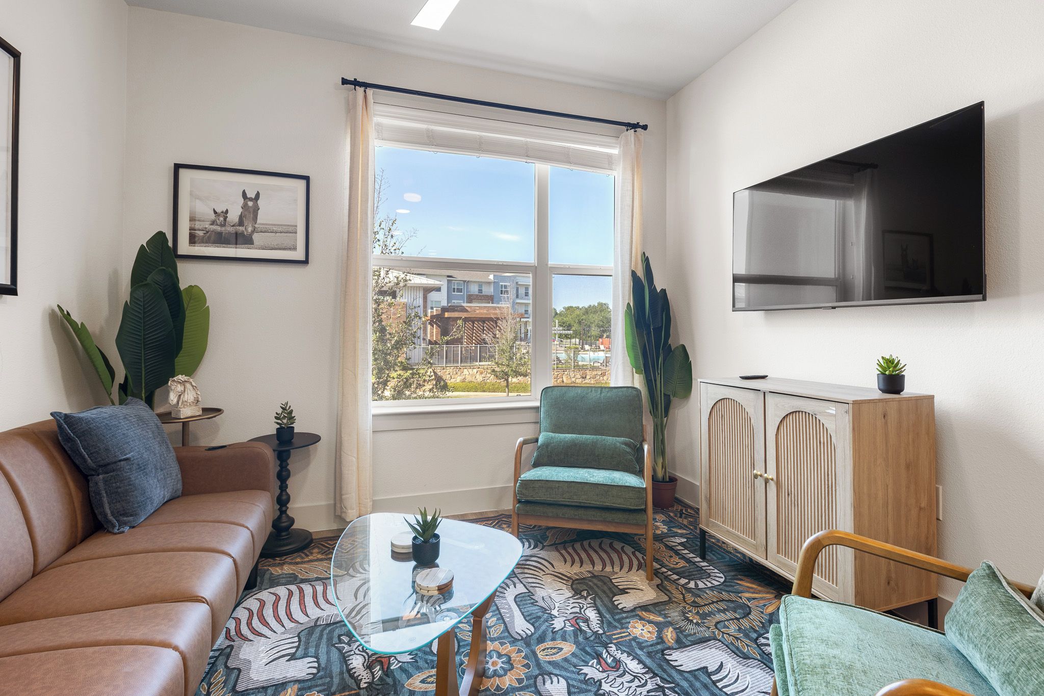 A furnished living room with a sofa, armchair, coffee table, and a TV mounted on the wall.