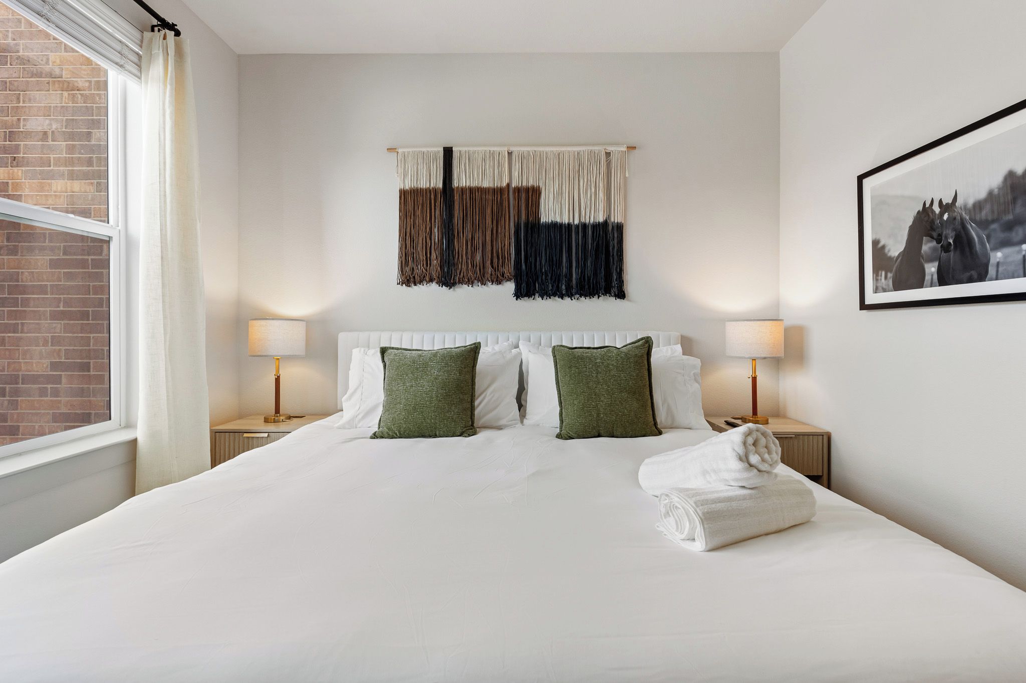 A hotel room with a large bed, two bedside tables with lamps, a wall-mounted tapestry, and a framed picture.