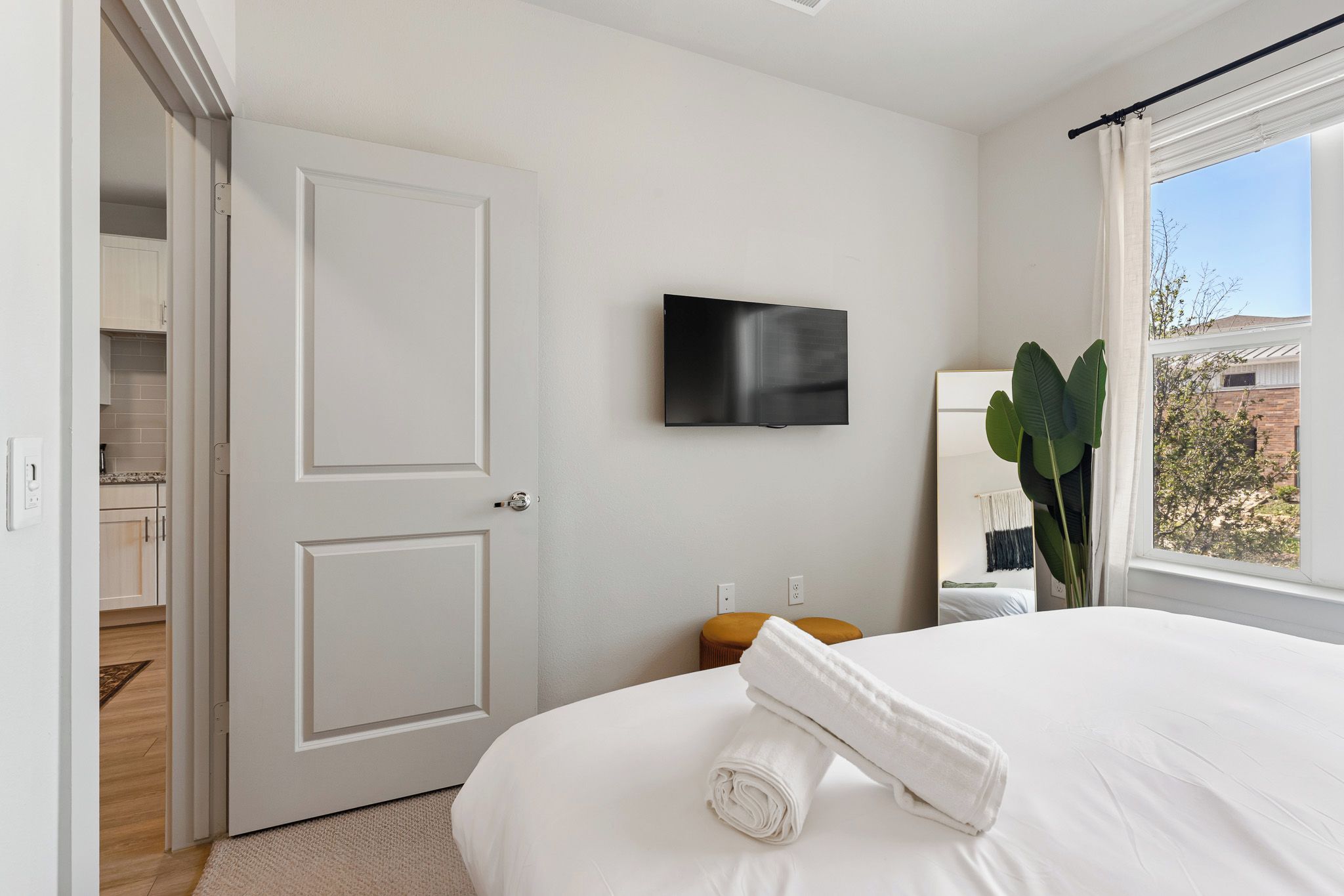 A hotel room with a bed, a flat-screen TV mounted on the wall, a window with a view of the outside, and a door leading to a bathroom.