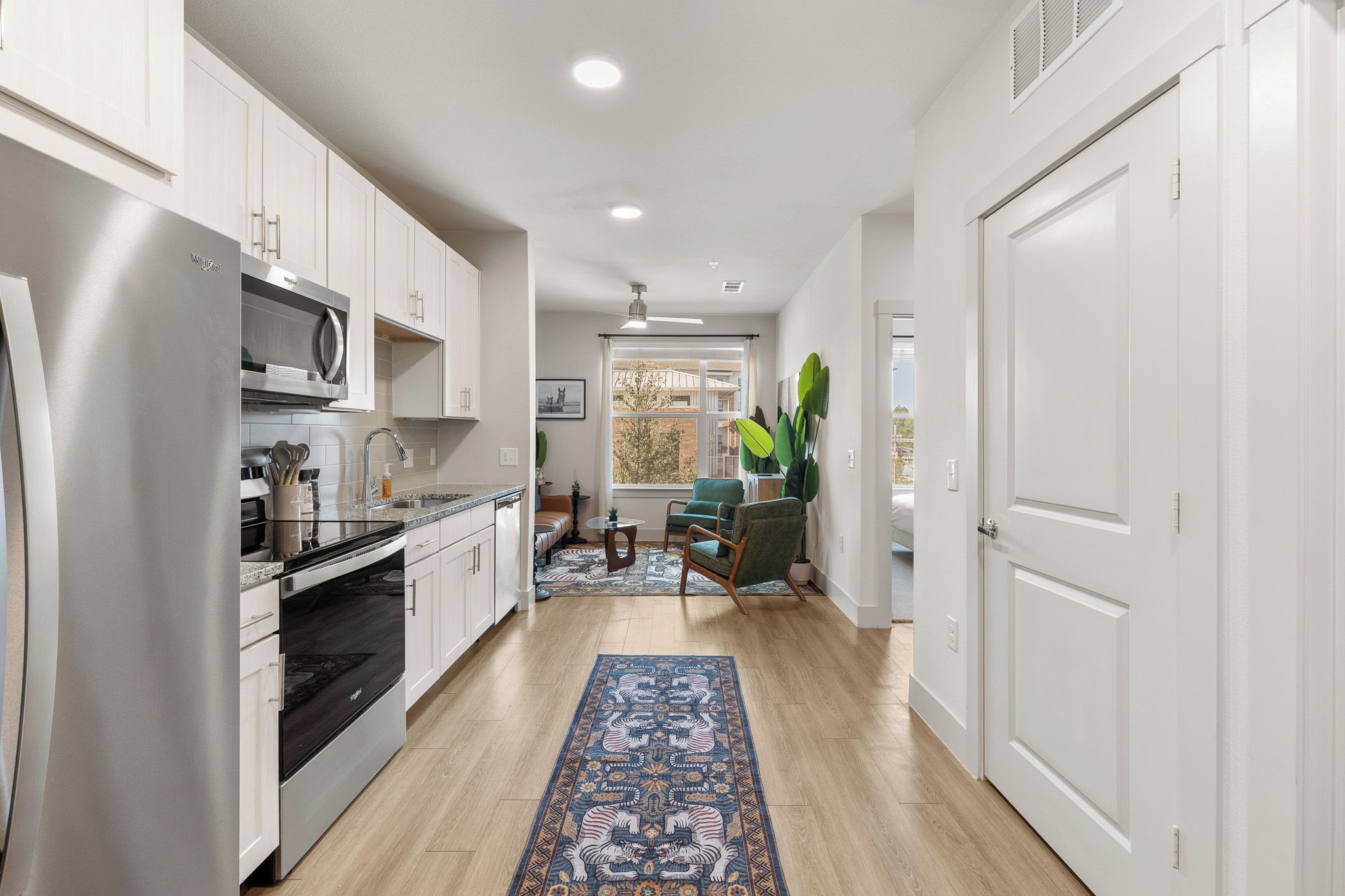 A modern kitchen with white cabinetry, stainless steel appliances, and a large window.