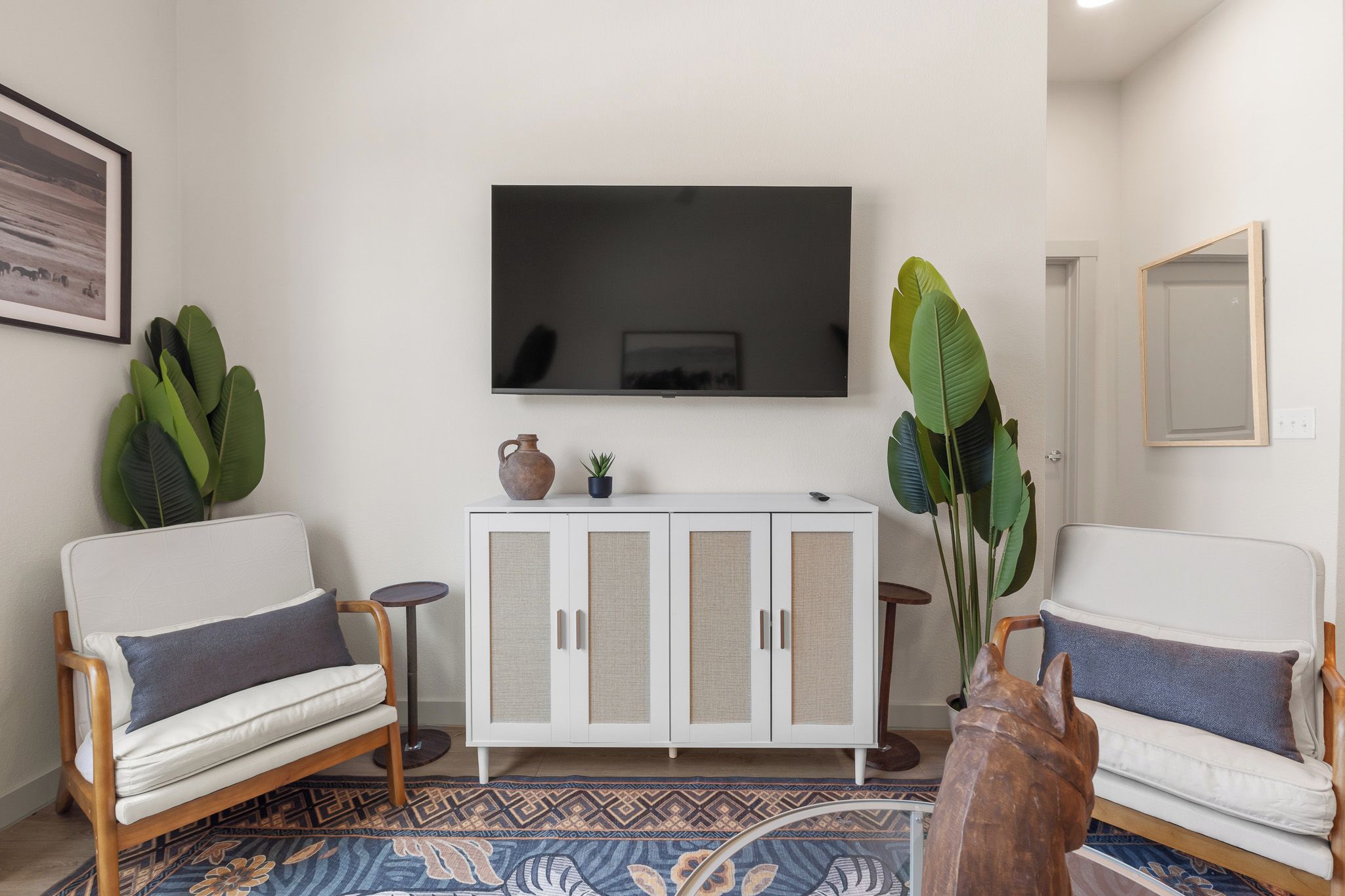 A living room with two sofas, a white cabinet, a flat-screen TV, and large green plants.