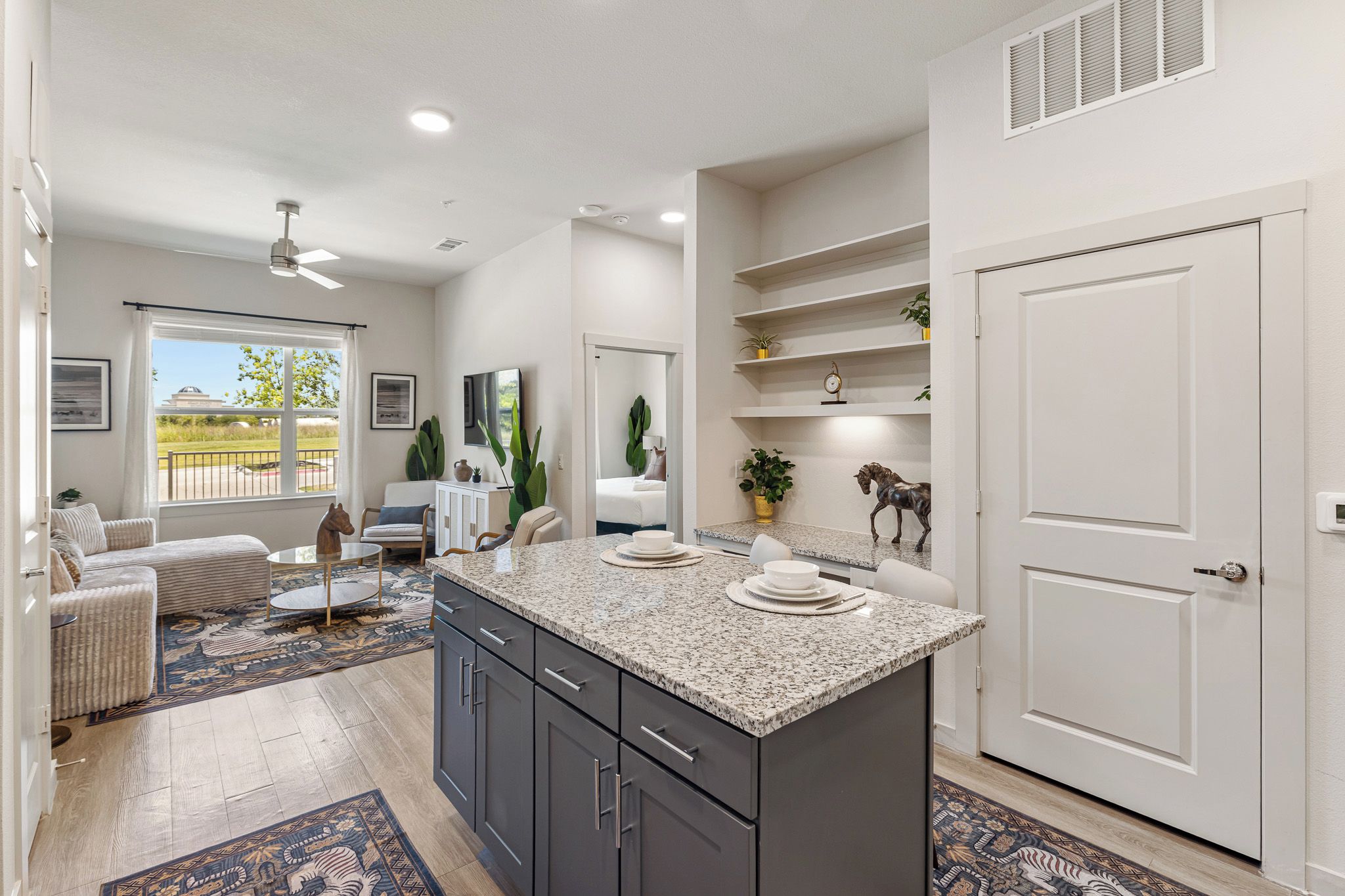 A modern kitchen with a granite countertop, dark cabinets, and a dining area with a patterned rug.