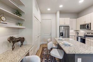 A modern kitchen with white cabinetry, a stainless steel refrigerator, a microwave, and a coffee maker.