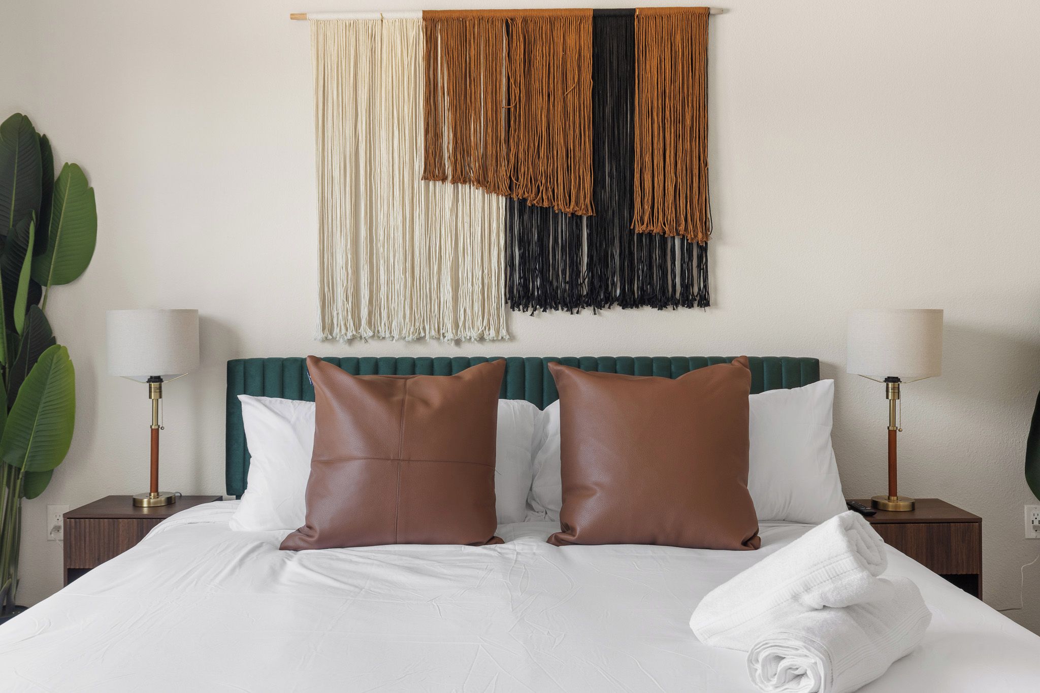 A hotel room with a bed, two nightstands, a wall-mounted macrame piece, and a potted plant.