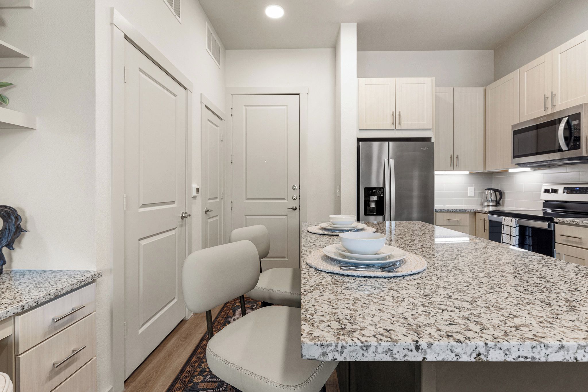 A modern kitchen with granite countertops, stainless steel appliances, and a seating area with chairs.