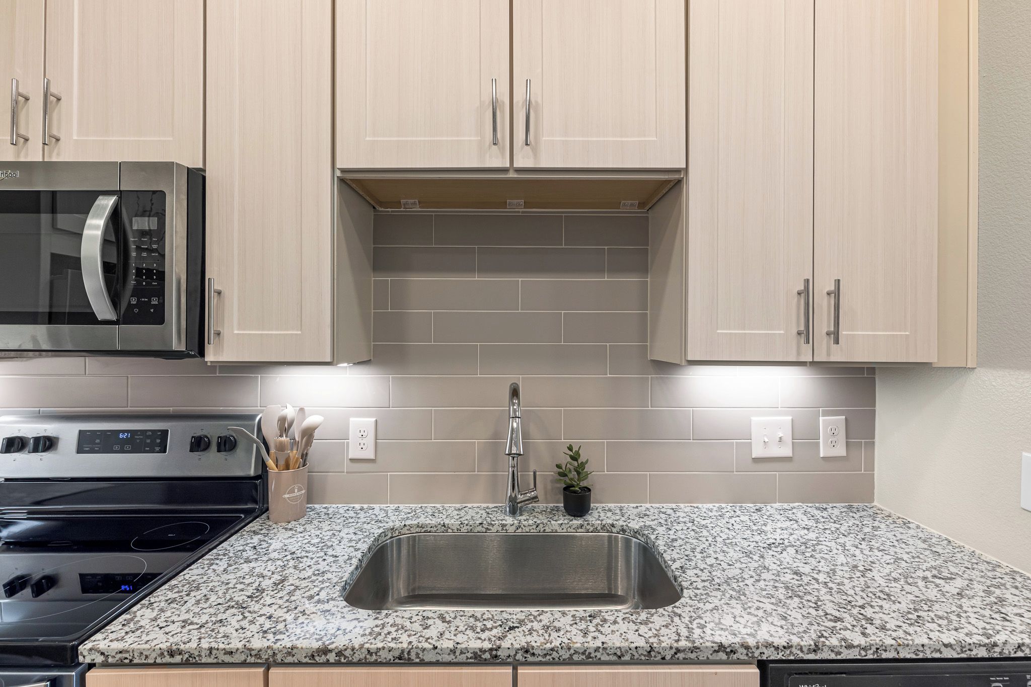 A kitchen with a stainless steel sink, granite countertop, and modern cabinetry.