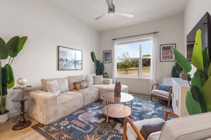 A spacious living room with a large sofa, a coffee table, and a view of the outdoors through a window. - Cozy Collin Square 1BR | Relax + Work CSA 5107 (McKinney)