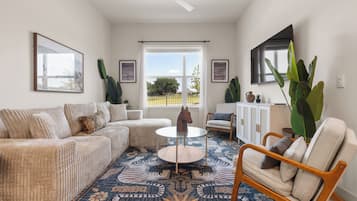 A living room with a sofa, armchair, coffee table, and a large plant.