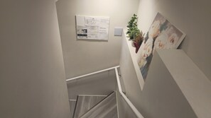 Een wenteltrap met een leuning, een plant aan de muur en een ingelijst kunstwerk.