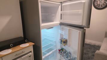 A compact refrigerator with a freezer compartment, a small freezer, and a shelf with beverages.