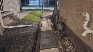 A pathway leading to a garage with a concrete surface and a small grassy area beside it. - New Modern 1BR Suite With Private Entrance - Easy Access To Malls (Winnipeg)