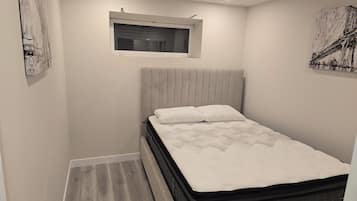 A small, neatly arranged bedroom with a single bed, a window, and artwork on the walls.