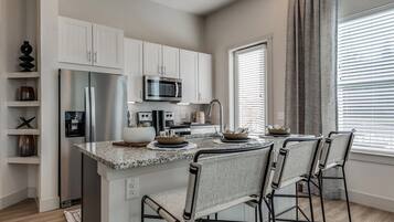 A modern kitchen with white cabinets, stainless steel appliances, a granite countertop, and bar stools.