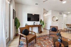 Ein Wohnzimmer mit Fernseher, zwei Ledersesseln, einem Holztisch und einem gemusterten Teppich.