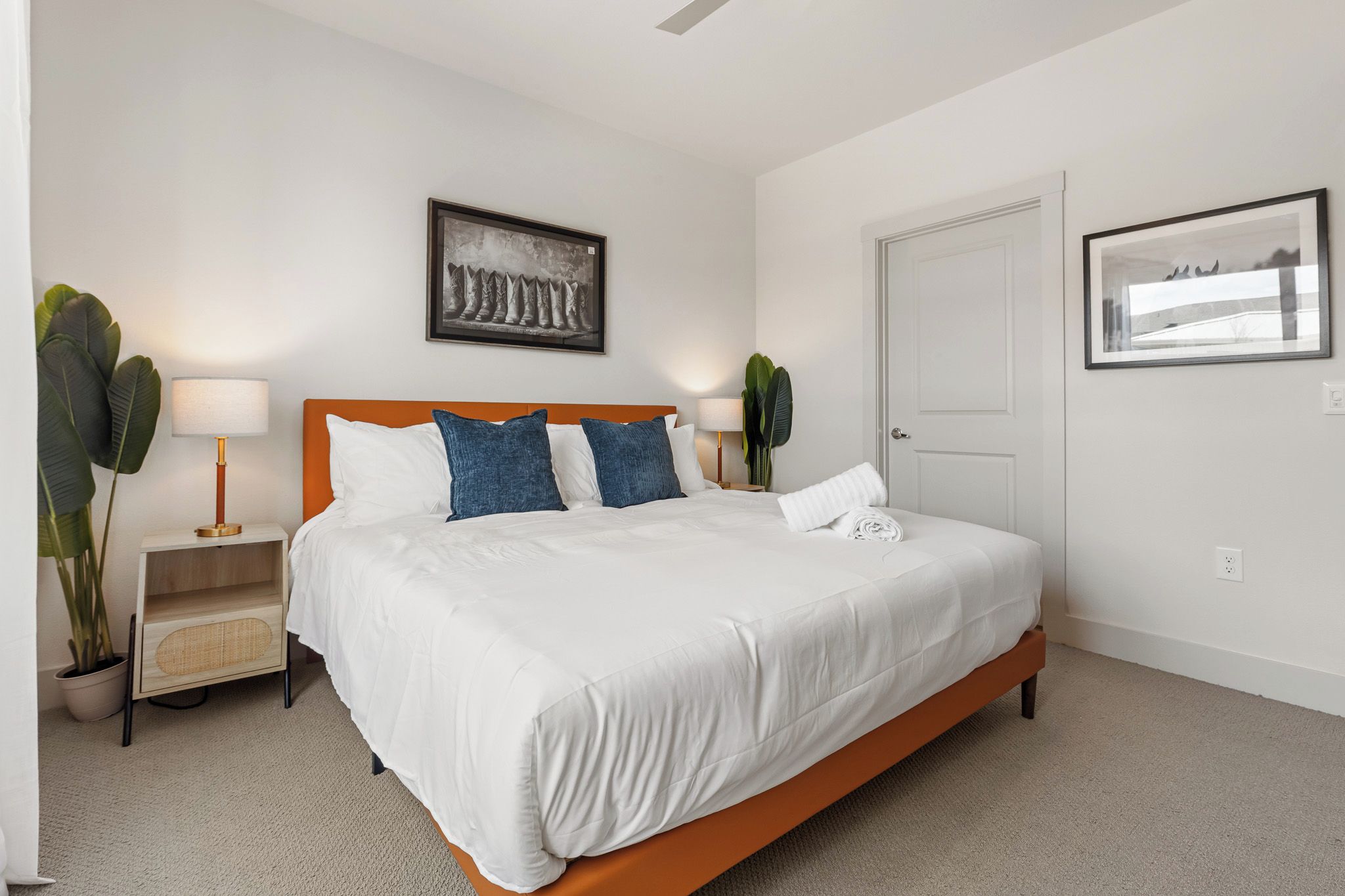 A bedroom with a bed, bedside tables, lamps, a door, and two wall-mounted pictures.