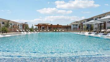 A swimming pool with lounge chairs, a covered area, and buildings in the background.
