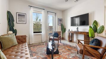A living room with a leather sofa, a glass coffee table, and a TV mounted on the wall.