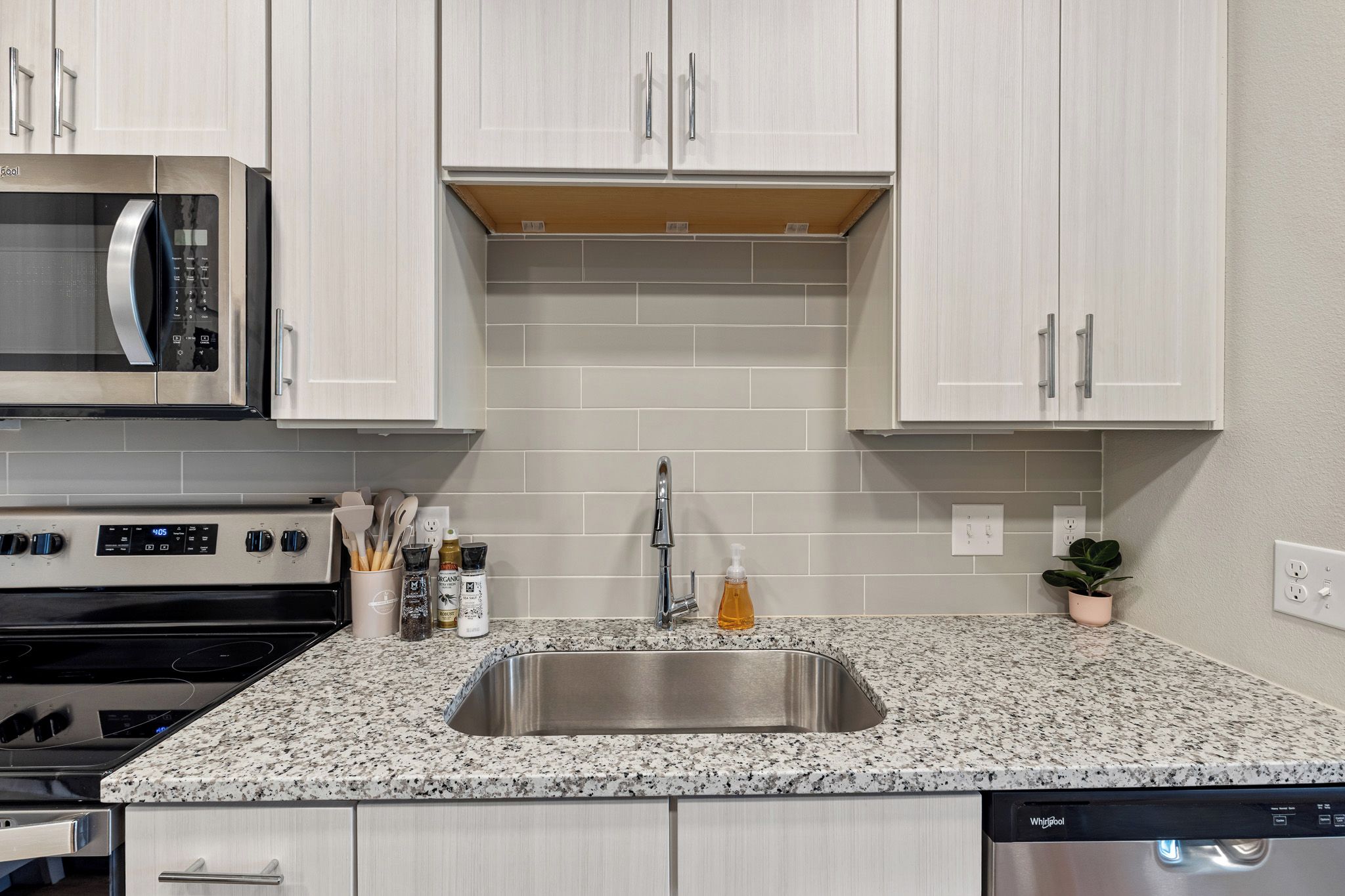 A kitchen with white cabinets, a stainless steel sink, granite countertop, and a microwave.