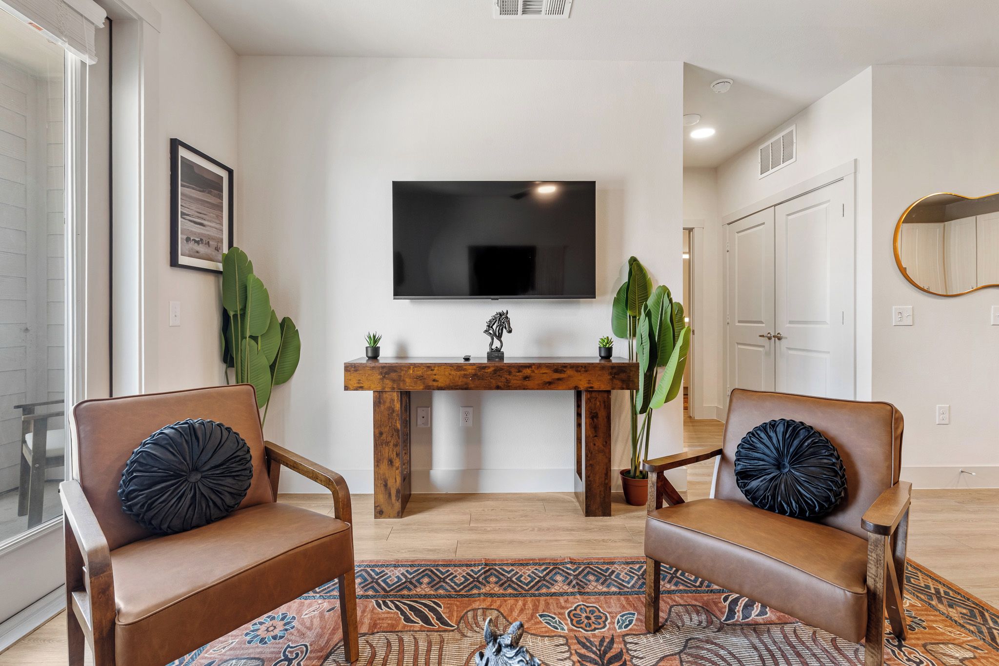 Un salon moderne avec deux fauteuils en cuir, une table basse en bois, un téléviseur à écran plat et un tapis à motifs.