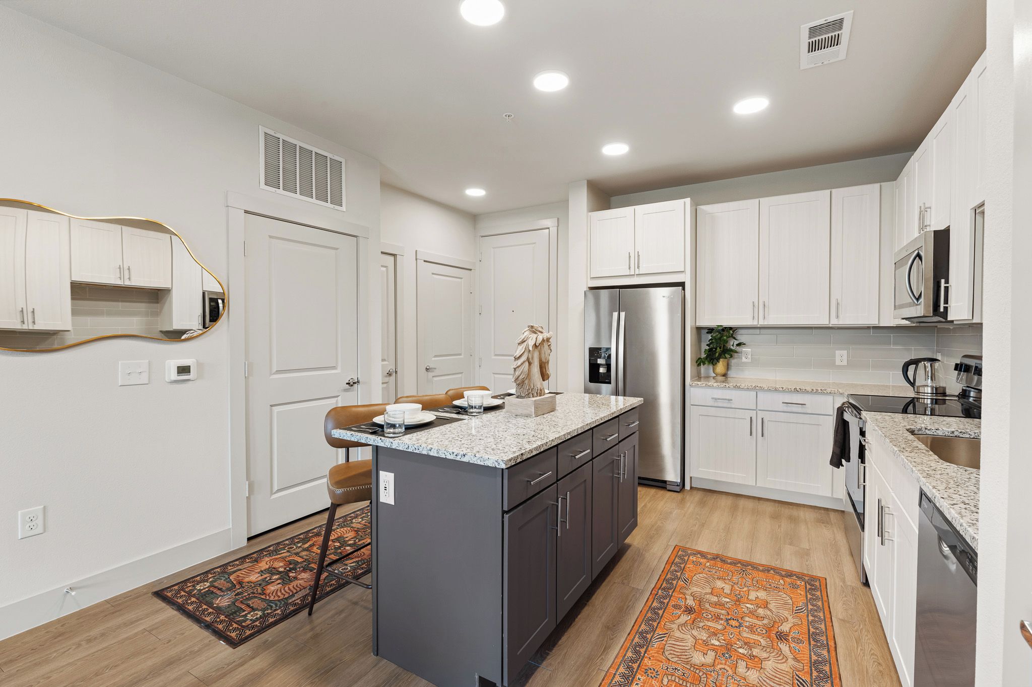 A modern kitchen with white cabinetry, a central island, stainless steel appliances, and a patterned rug.