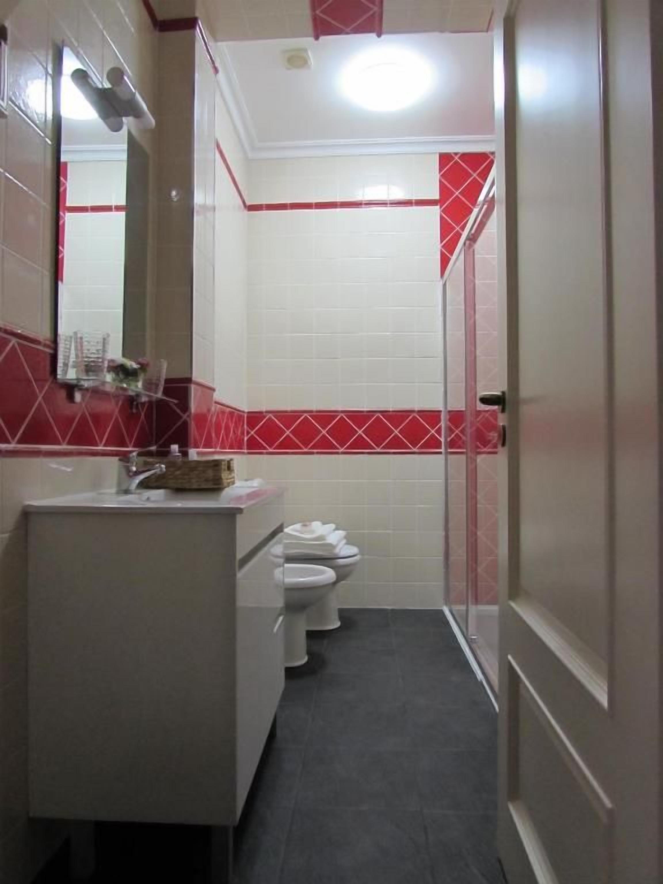 Un baño estrecho con un lavamanos blanco, dos inodoros y un espejo.