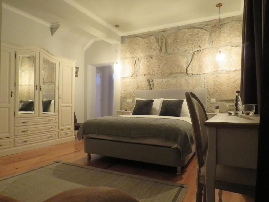 A bedroom with a bed, a dresser, a desk, and a stone wall.
