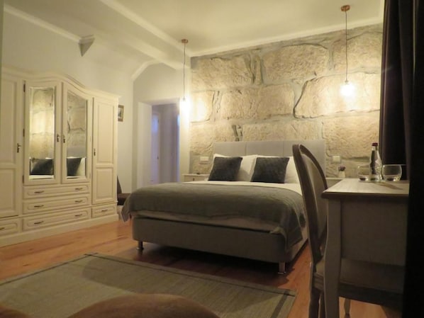 Un dormitorio con cama, cómoda, escritorio y pared de piedra.