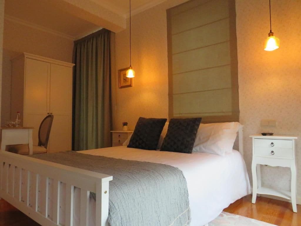 Un dormitorio con cama, mesita de noche, armario y ventana con cortinas.