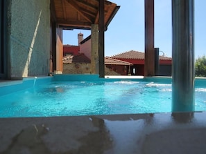 Una piscina con agua azul cristalina, rodeada por un edificio con tejado de azulejos y una estructura de madera superior.