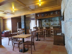 Interior de restaurante con mesas y sillas de madera, una zona de bar con estantes llenos de botellas y una pared de piedra.