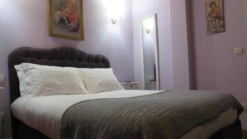 A bedroom with a large bed, a nightstand, a dresser, and a mirror.