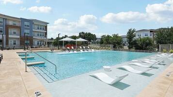 A swimming pool with lounge chairs and umbrellas, surrounded by buildings.