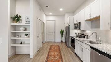 A modern kitchen with white cabinetry, stainless steel appliances, and a wooden floor.