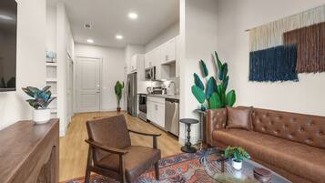 A modern living room with a brown leather sofa, a wooden chair, a glass coffee table, and a patterned rug.